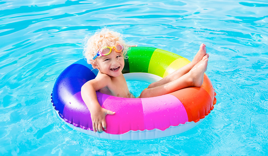 Un niño flota feliz en una piscina sobre un salvavidas a rayas de arco iris. 