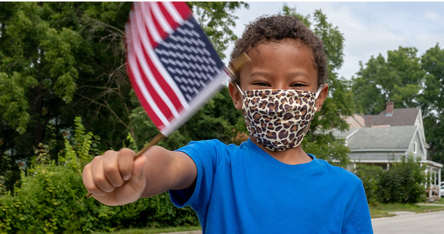  Un niño ondea una bandera estadounidense con una máscara puesta.