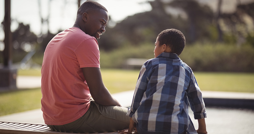 An African American father speaks with his son on a bench. 