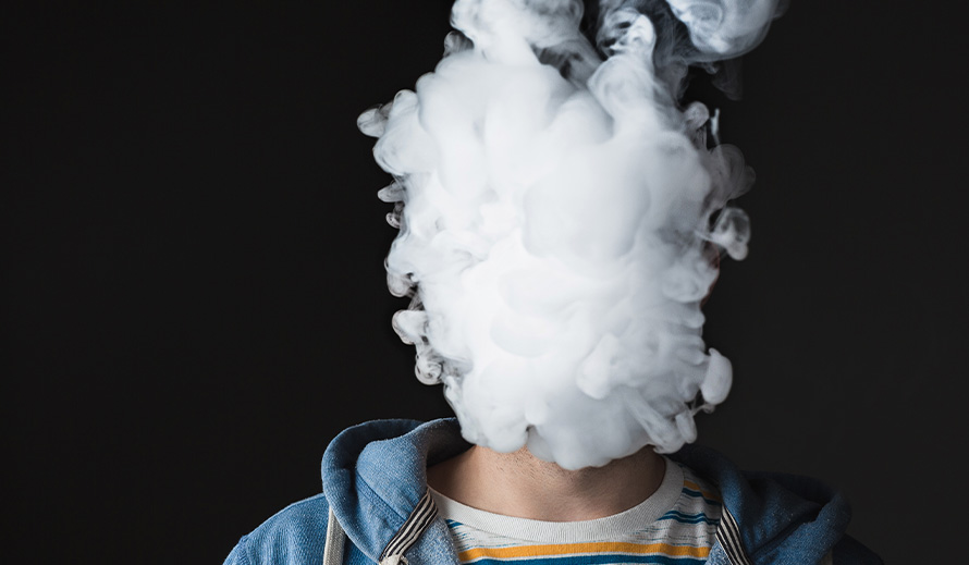 El humo de un cigarrillo electrónico cubre por completo la cara de un adolescente. 
