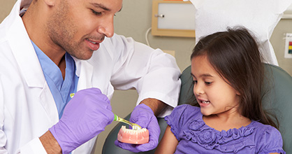 Dentist showing a little girl how to brush her teeth