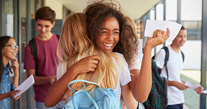 High school students happily hugging each other, with acceptance letters in their hands
