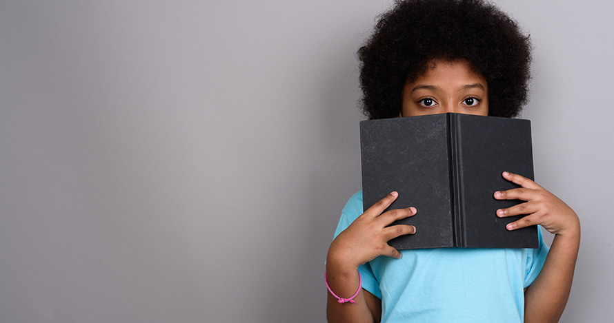Una tímida niña afroamericana se esconde detrás de un libro.