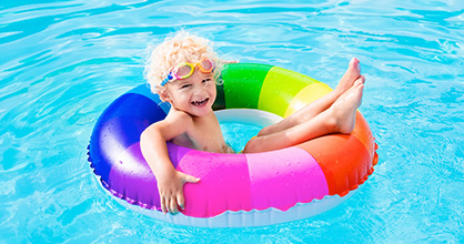Happy little boy on a rainbow-striped floatie in a swimming pool.