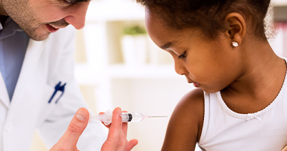  Un pediatra está a punto de administrar una vacuna a una niña afroamericana.